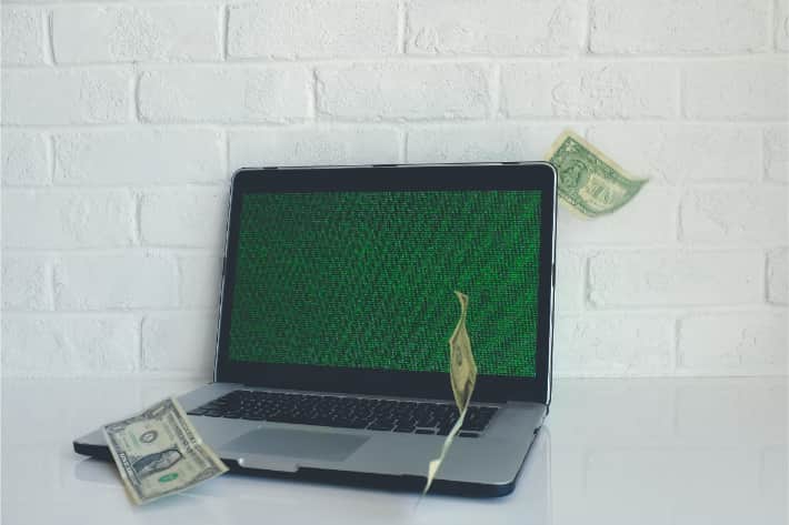 Un laptop hackerato, con banconote americane da un dollaro che cadono su di esso
