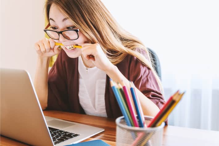Donna che mordicchia una matita davanti al proprio laptop, in segno di frustrazione