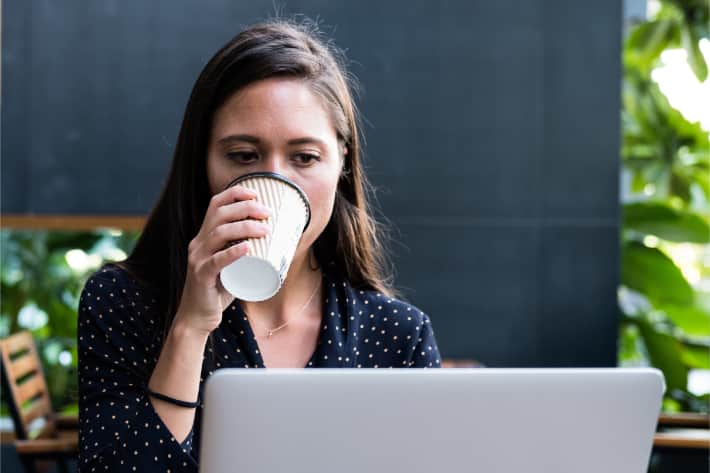 Una donna naviga con il proprio laptop sorseggiando un caffè