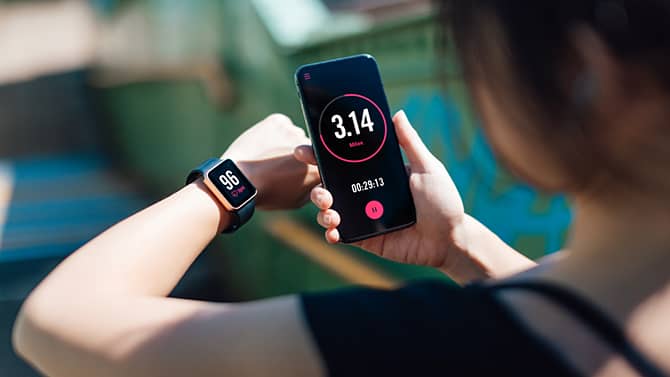 Donna che utilizza un'app per il fitness sullo smartphone e sullo smartwatch. Le app per monitorare l'attività fisica sono un esempio dei potenziali effetti positivi della tecnologia sulla salute.
